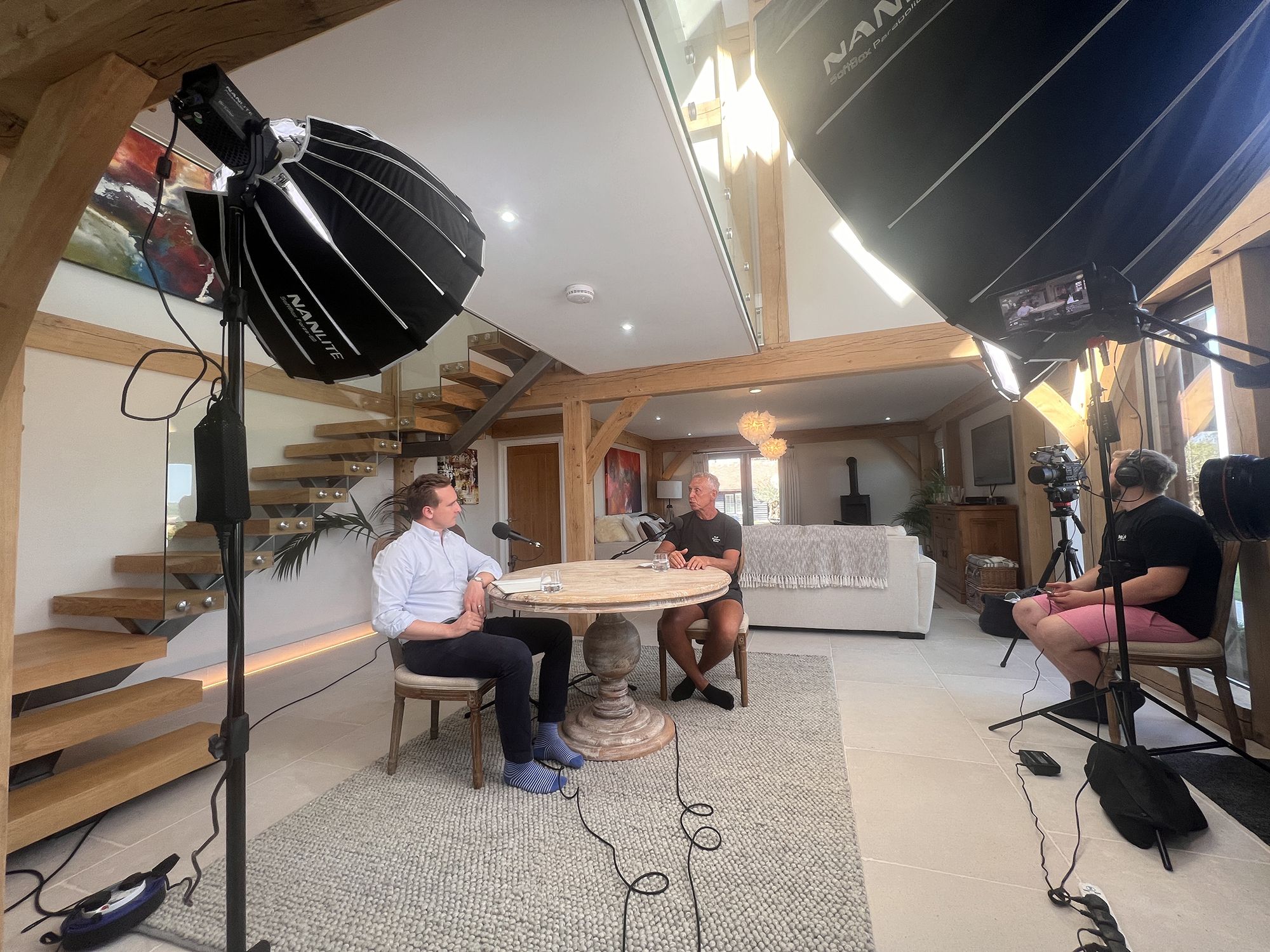 People sat around a table with cameras and lights, recording a podcast. 